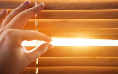 Looking through window blinds, sun light coming inside.