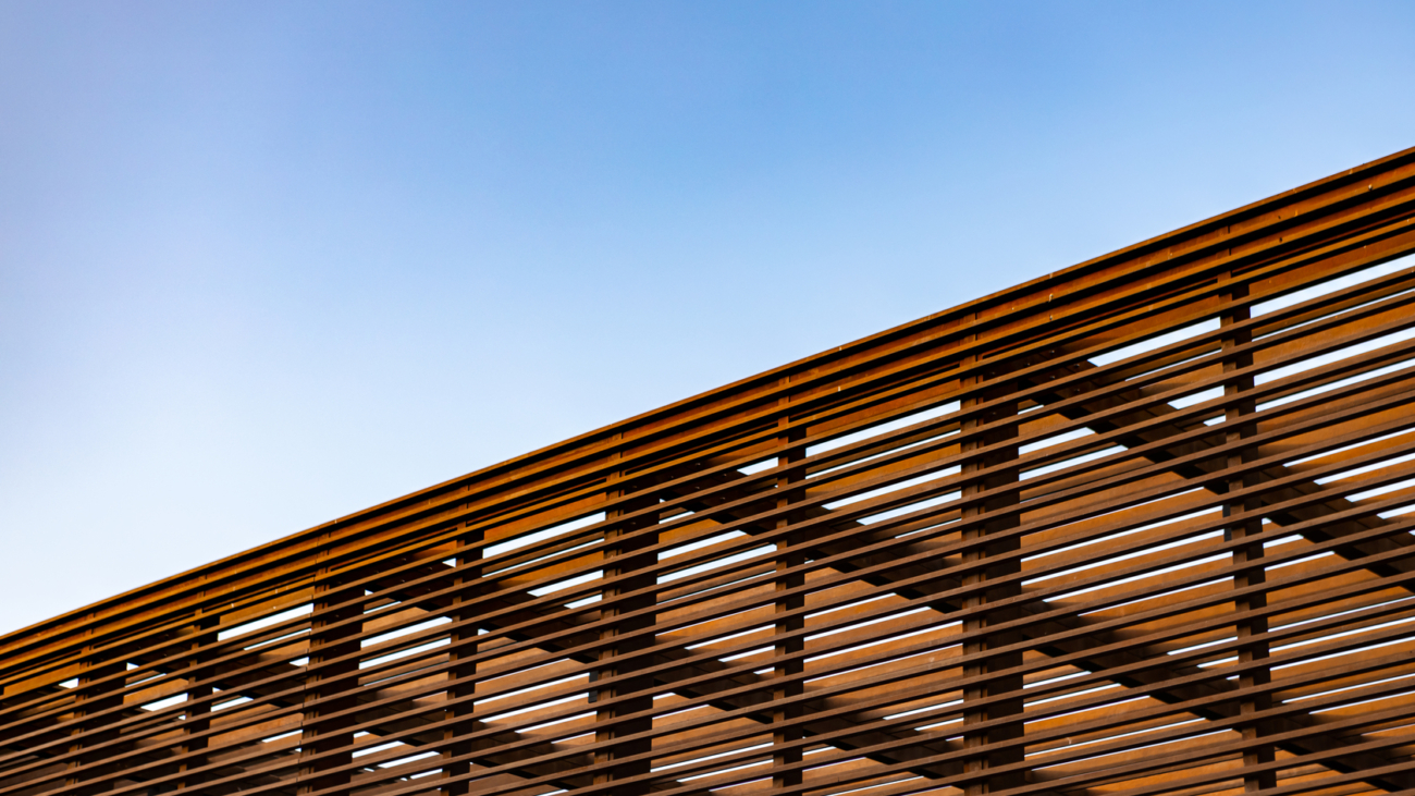 Wooden slat shading structure with roof against blue sky